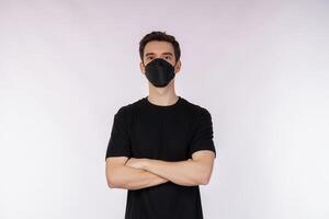 Portrait of young handsome man wearing medical mask and black t-shirt, standing with crossed arms with isolated on studio white background photo