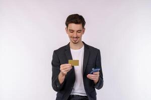 Portrait of happy young businessman standing using mobile cell phone and holding credit bank card isolated on white color background studio photo