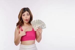 Portrait of excited young woman holding bunch of dollars banknotes and pointing finger at money isolated over white background photo