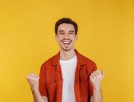 Portrait of happy joyful young man standing doing winner gesture clenching fists keeping isolated on yellow color wall background studio