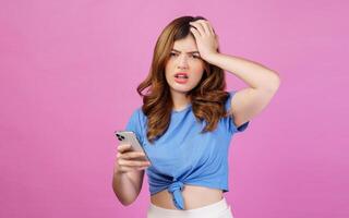 Portrait of confused young woman wearing casual t-shirt using smartphone isolated over pink background photo