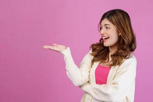 Portrait of Surprised young woman presenting or showing open hand palm with copy space for product over isolated pink background photo