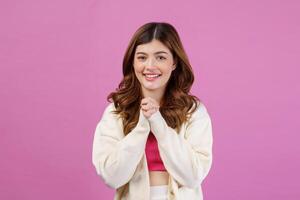 Portrait of Smiling young woman praying with folded hand or making a wish isolated over pink background photo