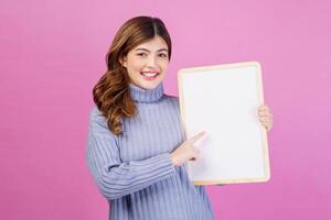 Portrait of Happy young woman holding an empty white placard over isolated pink background. photo