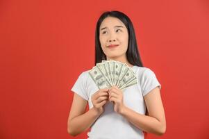 Portrait of a cheerful young woman holding money banknotes and celebrating isolated over red background photo