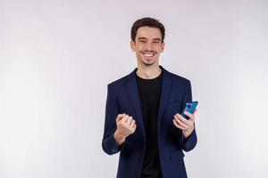 Portrait of a happy businessman using smartphone and doing winner gesture clenching fist over white background photo