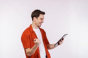 Portrait of attractive cheerful man doing winner gesture clenching fist and using device app searching web isolated over white color background photo