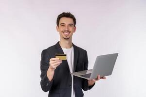 Portrait of young handsome smiling businessman holding creadit card and laptop in hands, typing and browsing web pages isolated on white background photo