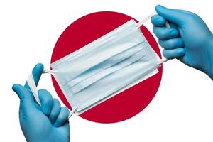 Medic holding respiratory face mask in hands in blue gloves on background flag of flag of Japan or Japanese flag photo