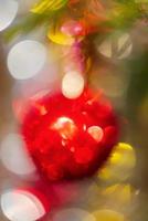 Defocused red Xmas ball hanging on branch of pine tree. Creative Christmas colorful abstract blurred bokeh