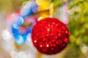 Defocused shining red Christmas ball hanging on branch of Xmas pine tree. Colorful creative abstract blurred bokeh photo