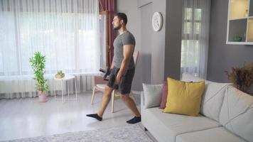 Young man exercising at home is training with dumbbells. Fit man does forward lunge exercises at home in his spacious and bright apartment with minimalist interior. video