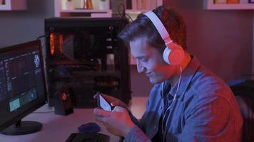 joven hombre En Vivo transmisión y jugando móvil juego en teléfono inteligente a hogar. joven hombre jugando vídeo juegos en computadora y teléfono. video