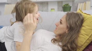 madre y hija acostado abajo, abrazando cada otro. contento madre y hija acostado en sofá hablando y riendo con cada otro. video