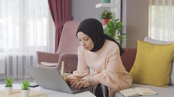 alunno giovane musulmano ragazza Lavorando su il computer portatile a casa. musulmano adolescenziale ragazza Lavorando su il computer portatile a casa e assunzione Appunti nel libro. video