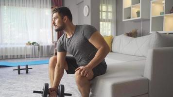 sterk atletisch Mens oefenen Bij huis, opleiding met halters. mannetje aan het doen opdrachten in leven kamer Bij huis en werken spieren met zwaar halter gewichten. video