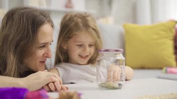 The girl throws money into the boy's piggy bank and is happy. The mother saves money in the piggy bank for the future of her little daughter. video