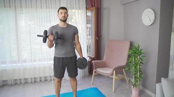 homme bodybuilder exercice avec haltères à maison. Masculin Faire des exercices dans vivant pièce à Accueil et travail muscles avec lourd haltère poids. video