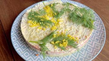 een vrouw is garnering een net gemaakt mimosa salade door sprenkeling het met geel ei dooier. video