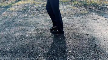 un' elegante donna di andatura nel largo gamba pantaloni su un' sentiero nel il parco contro il fondale di raggi di sole. video