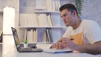 joven hombre trabajando a el computadora. joven trabajando en su computadora toma notas en su cuaderno. video