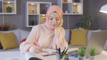 hembra musulmán estudiante estudiando utilizando ordenador portátil y libros. el hijab niña es preparando para el exámenes video