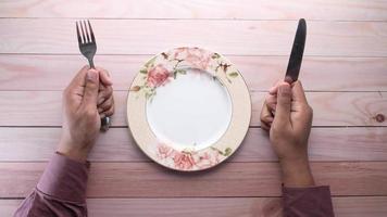 hand holding cutlery and empty plate on wooden background top down video