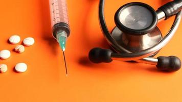 syringe, stethoscope and pills on orange background, close up