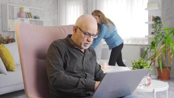 The daily life of the elderly couple. Elderly couple is at home, man is working with laptop and woman is cleaning. video