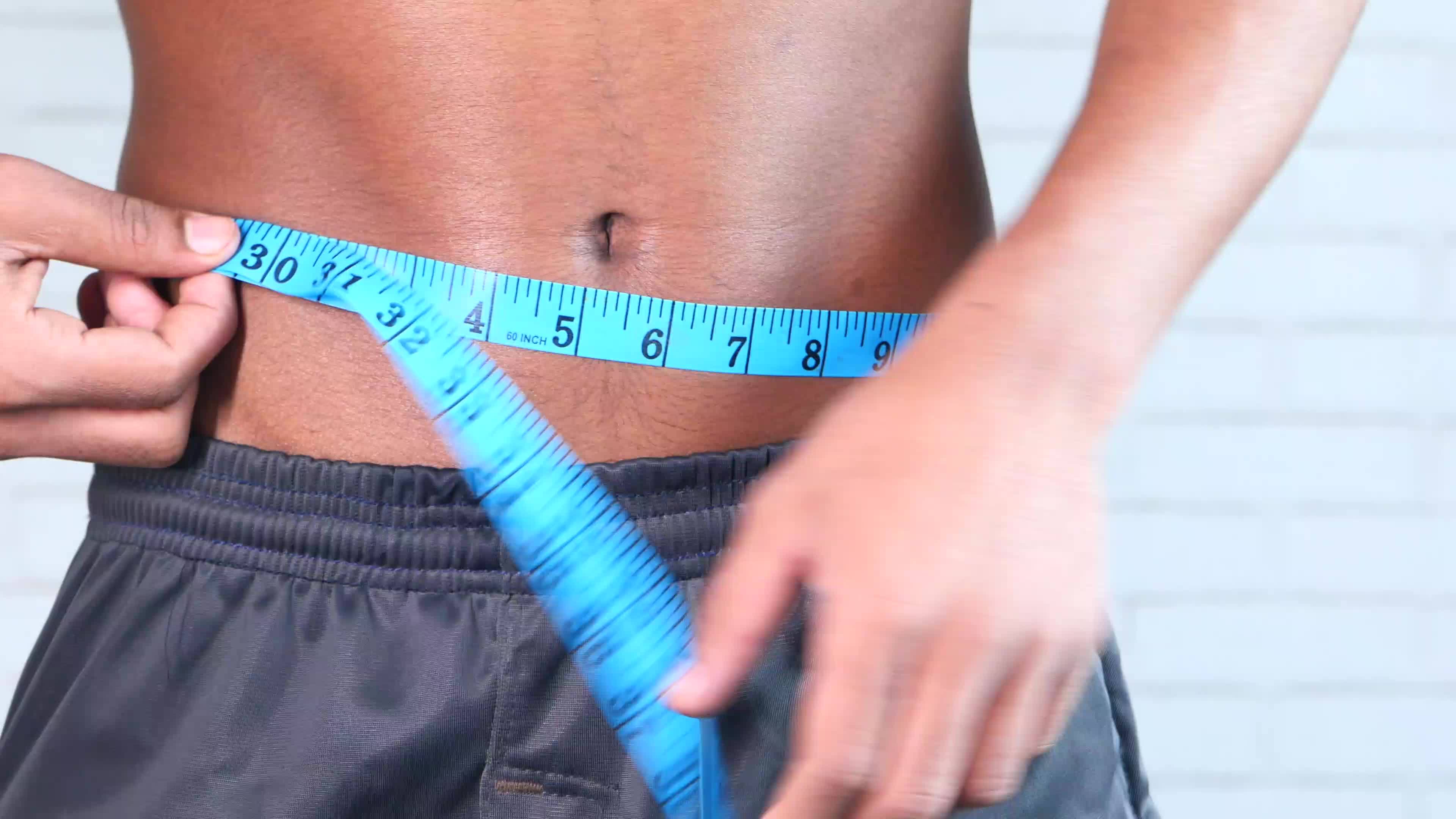 Young man measuring his waist with a tape measure, close up 21363073