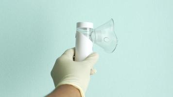 Hand in latex gloves holding nebulizer against light green background . video