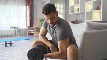 fare gli sport a casa. in forma uomo lavori su braccia con manubri. uomo esercizio nel vivente camera a casa e Lavorando muscoli con manubrio pesi. video