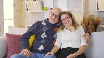 Happy and cute elderly couple looking at camera. Elderly couple sitting in their armchairs at home looking at camera and laughing. video