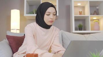 o negócio mulher vestindo uma lenço de cabeça é trabalhando dentro dela casa escritório. jovem hijab mulher olhando às computador portátil às casa e escrevendo alguma coisa em papel. video