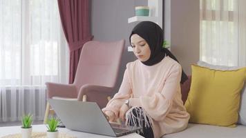Muslim teenage girl working on laptop at home. Muslim woman in hijab works with laptop. video