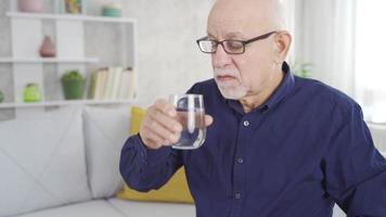 de oud Mens is nemen geneeskunde en lachend. de oud Mens drinken geneeskunde Bij huis is glimlachen op zoek Bij de camera. video