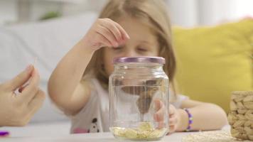 consapevole madre investire nel il futuro lanci oro in sua porcellino banca per sua figlia. cura genitore insegna ragazzo per Salva i soldi, pensare di futuro, gestire personale finanza, risparmi concetto. video