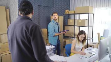 Business partners working together at the warehouse of an online store. Young businessman and businesswoman making online sales deliver orders to the courier man. video