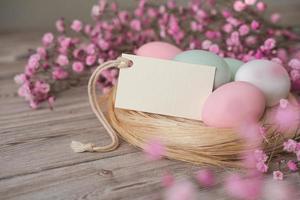 Nest with eggs in soft pastel colors and blank white card for text. Mockup tag. Easter card photo