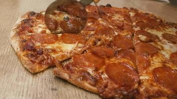 Top view of a man hand cutting pizza with a round cutter knife on the wooden table in the kitchen video