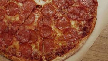 Top view shot of delicious pepperoni pizza with mozzarella cheese on wooden table in the kitchen. video