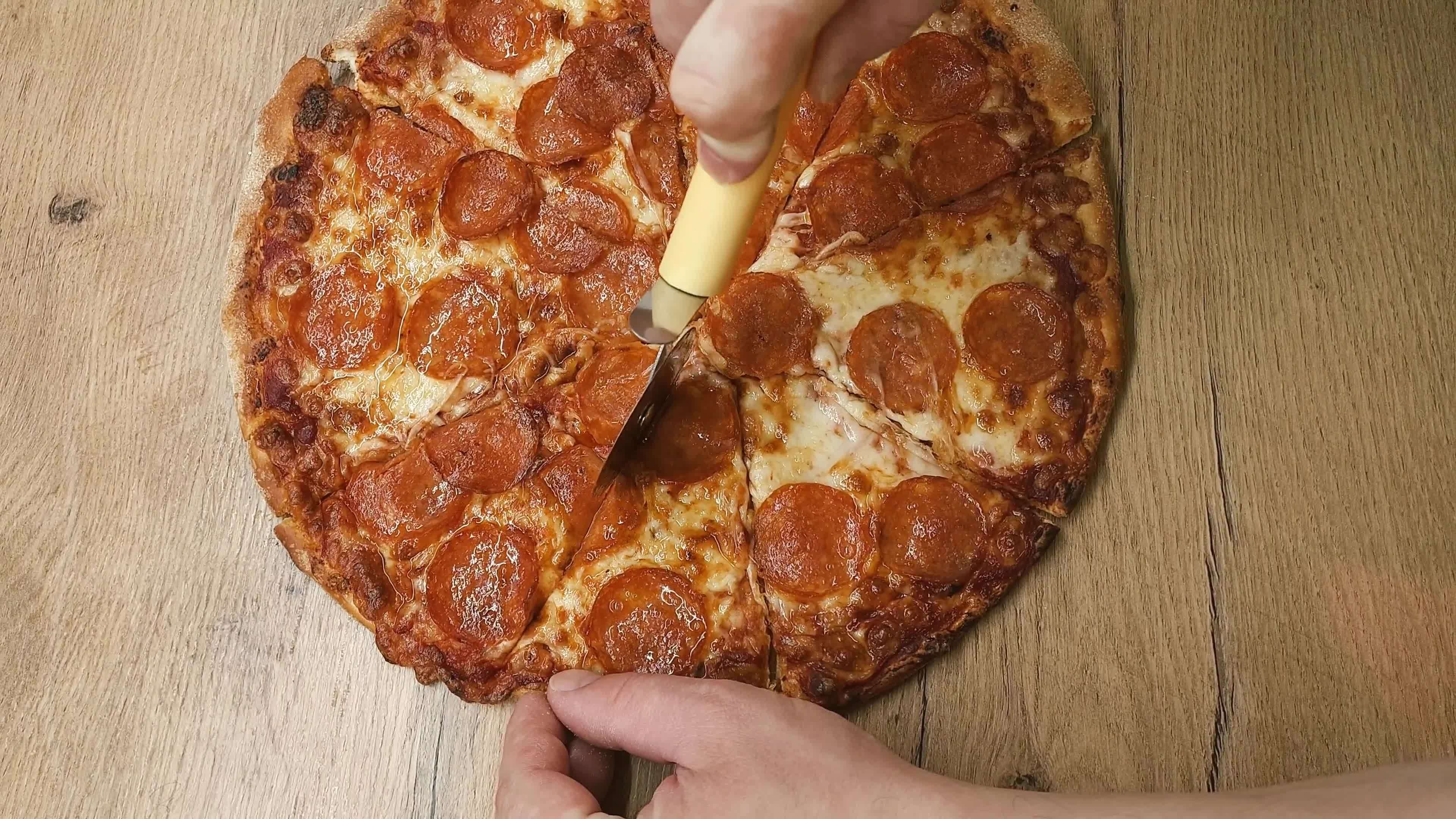 Top view of a man hand cutting pizza with a round cutter knife on the wooden table in the