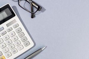 Flat lay of Calculator, pen and eyeglasses on gray background with Copy Space photo