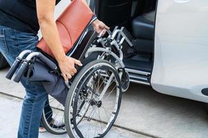 asiático invalidez mujer en silla de ruedas consiguiendo en su auto, accesibilidad concepto. foto