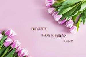 festive beautiful lilac background with fresh spring tulips and text in wooden letters of Happy Mother's Day. top view. flat styling. photo