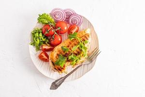 top view of the serving white plate with juicy grilled chicken fillet with fresh vegetables on a white background. a copy of the space. photo