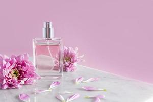 an elegant bottle of cosmetic spray stands on part of a white marble podium with chrysanthemum flowers. pink background. a copy space.