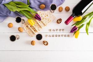 silver glasses with red wine, matzah, a bottle of wine and tulips on a white wooden background. wooden letters Passover photo