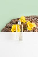 a transparent bottle of cosmetic spray lies on parts of a white textured podium and bark of a tree with yellow tulips. vertical view. copy space. photo