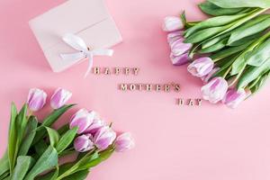 a festive composition with purple tulips and text in wooden letters of Happy Mother's Day. top view. flat styling. pink background. photo